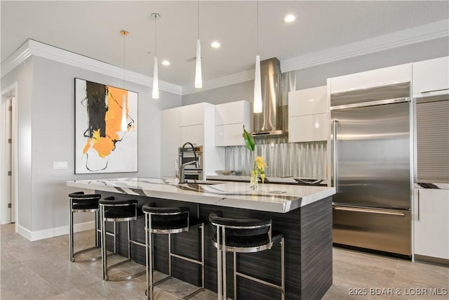 kitchen featuring a sink, ornamental molding, built in fridge, wall chimney range hood, and modern cabinets