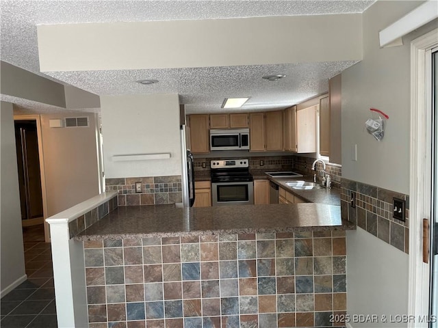 kitchen with a textured ceiling, stainless steel appliances, dark tile patterned floors, a sink, and visible vents