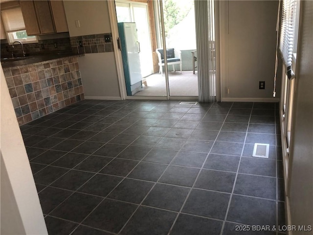 empty room featuring dark tile patterned floors, a sink, visible vents, and baseboards