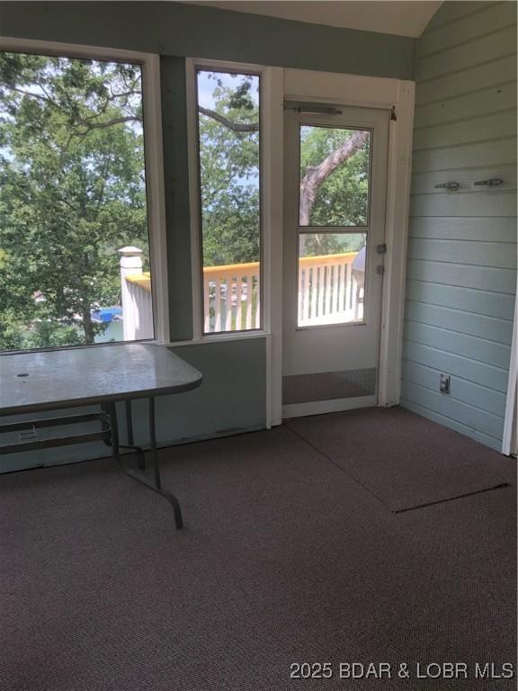 doorway to outside with lofted ceiling and wood walls