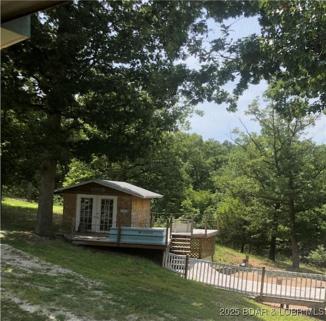 view of home's exterior featuring french doors, a lawn, a deck, stone siding, and an outdoor structure