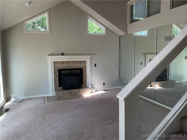 unfurnished living room with carpet, visible vents, a premium fireplace, high vaulted ceiling, and baseboards