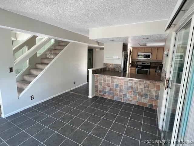 kitchen featuring dark countertops, appliances with stainless steel finishes, open floor plan, a textured ceiling, and dark tile patterned floors