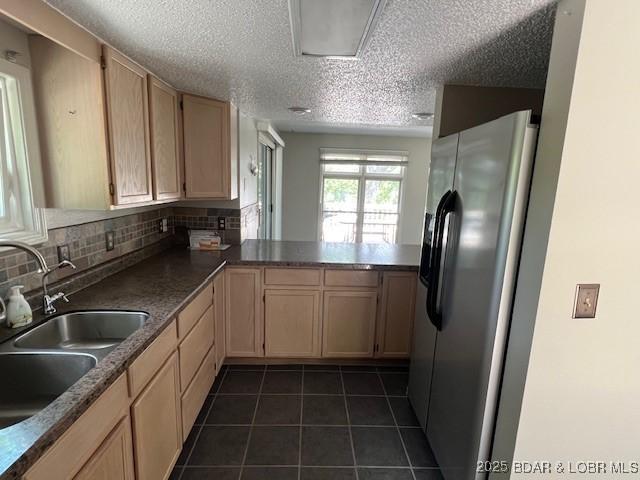 kitchen featuring stainless steel refrigerator with ice dispenser, backsplash, light brown cabinetry, a sink, and dark tile patterned floors