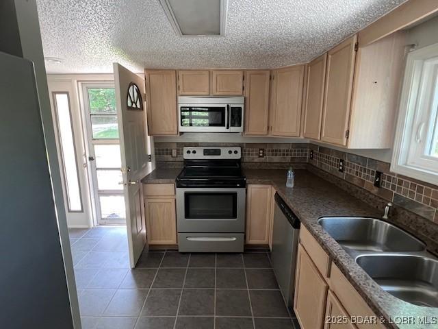 kitchen with appliances with stainless steel finishes, light brown cabinets, a sink, and tasteful backsplash