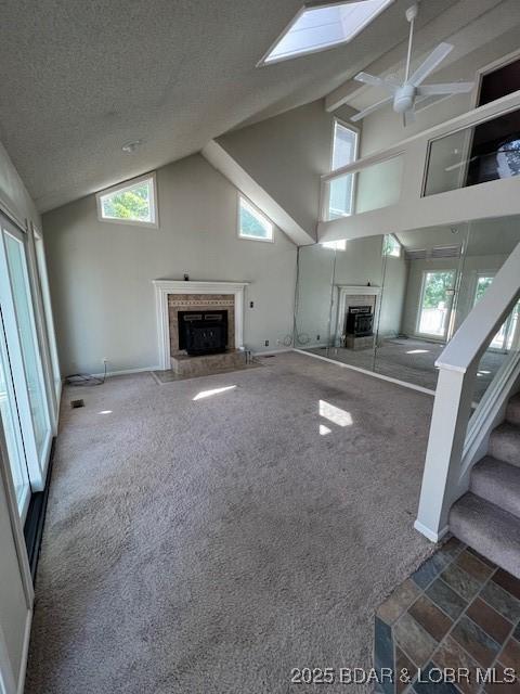 unfurnished living room with a textured ceiling, a skylight, a fireplace, carpet flooring, and stairs