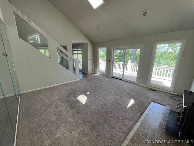 unfurnished living room with carpet floors, high vaulted ceiling, and baseboards