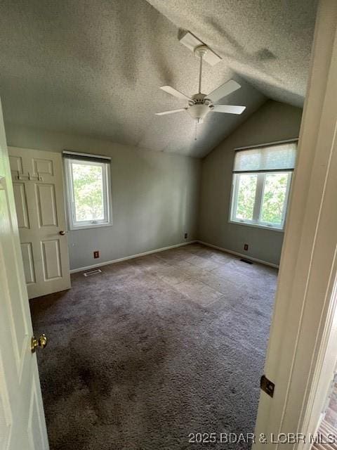 empty room featuring a textured ceiling, baseboards, vaulted ceiling, and carpet flooring