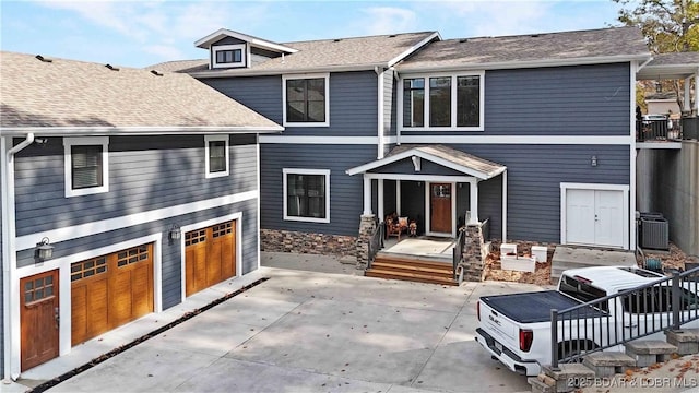 back of property featuring a garage, cooling unit, and roof with shingles