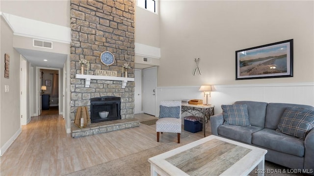 living area with a towering ceiling, a fireplace, wood finished floors, and visible vents