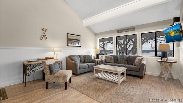 living room with vaulted ceiling with beams, plenty of natural light, wood finished floors, and wainscoting