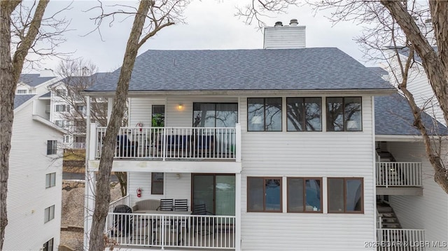 rear view of house featuring a shingled roof, a chimney, and a balcony