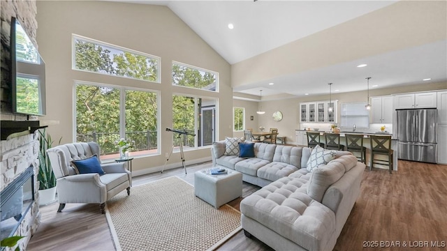 living area with high vaulted ceiling, a stone fireplace, wood finished floors, and recessed lighting