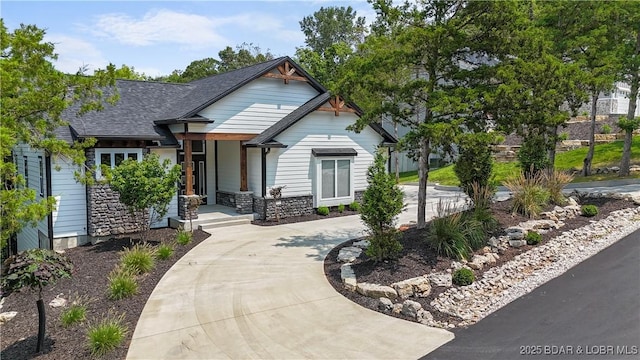 craftsman house with stone siding, concrete driveway, and roof with shingles