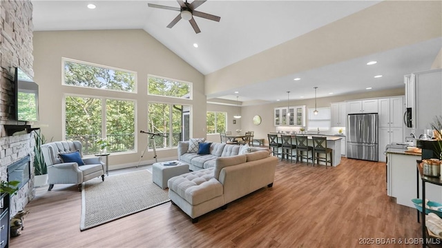 living room with recessed lighting, high vaulted ceiling, wood finished floors, and a stone fireplace