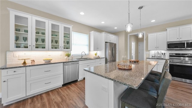 kitchen featuring a sink, white cabinetry, a kitchen breakfast bar, appliances with stainless steel finishes, and glass insert cabinets