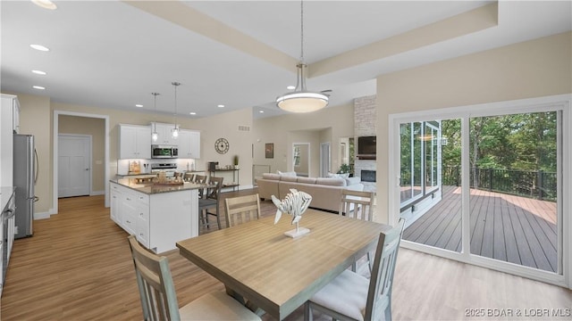 dining room with light wood-type flooring, baseboards, a raised ceiling, and recessed lighting