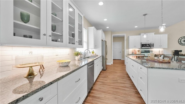 kitchen with a center island, stainless steel appliances, stone countertops, glass insert cabinets, and a sink