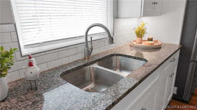 details featuring dark stone counters, tasteful backsplash, a sink, and white cabinetry