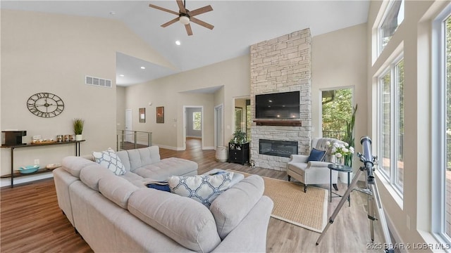 living area featuring a wealth of natural light, visible vents, a stone fireplace, and wood finished floors