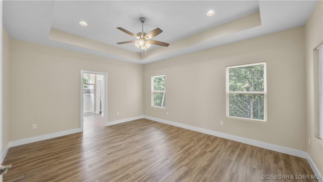 empty room featuring baseboards, a raised ceiling, and wood finished floors