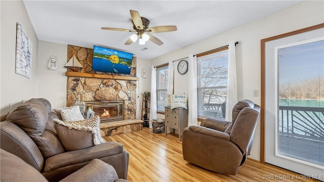 living area featuring a fireplace, light wood-style flooring, and a ceiling fan