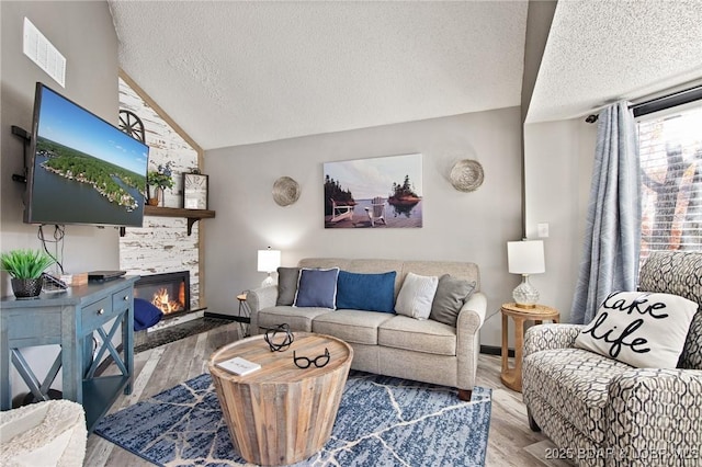 living area featuring lofted ceiling, visible vents, a fireplace, and wood finished floors