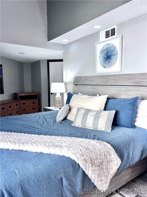 bedroom with visible vents, a textured ceiling, and wood finished floors