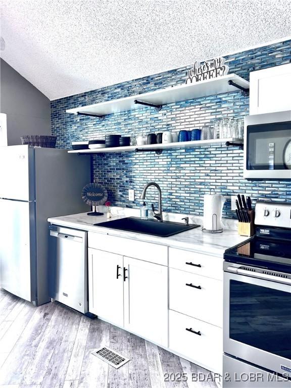 kitchen featuring visible vents, appliances with stainless steel finishes, white cabinetry, open shelves, and a sink