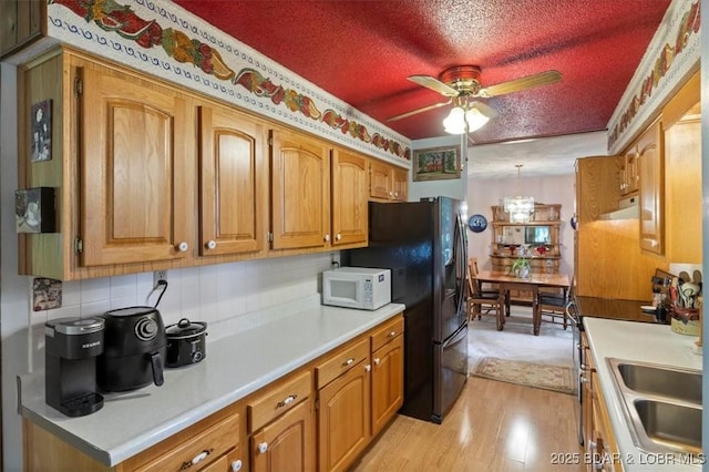 kitchen with a textured ceiling, white microwave, brown cabinetry, and light wood-style floors