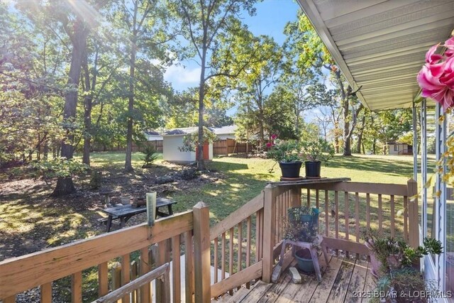 wooden terrace featuring a storage unit, a lawn, an outdoor structure, and fence