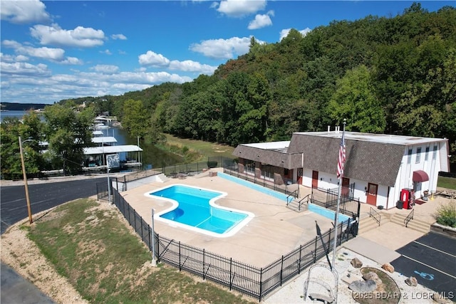 pool with fence, a wooded view, and a patio