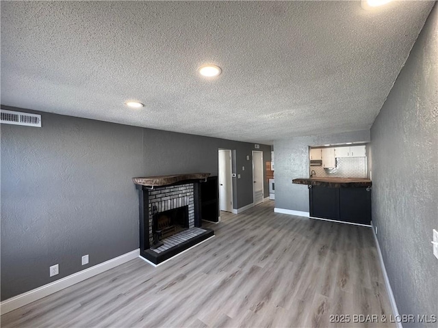 unfurnished living room with a fireplace, visible vents, a textured wall, wood finished floors, and baseboards