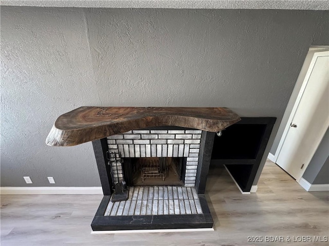 room details featuring a brick fireplace, a textured wall, baseboards, and wood finished floors