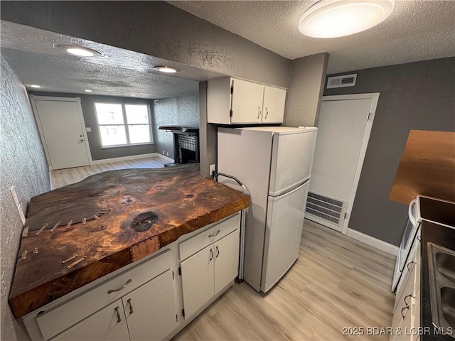 kitchen with visible vents, light wood finished floors, a textured ceiling, and freestanding refrigerator