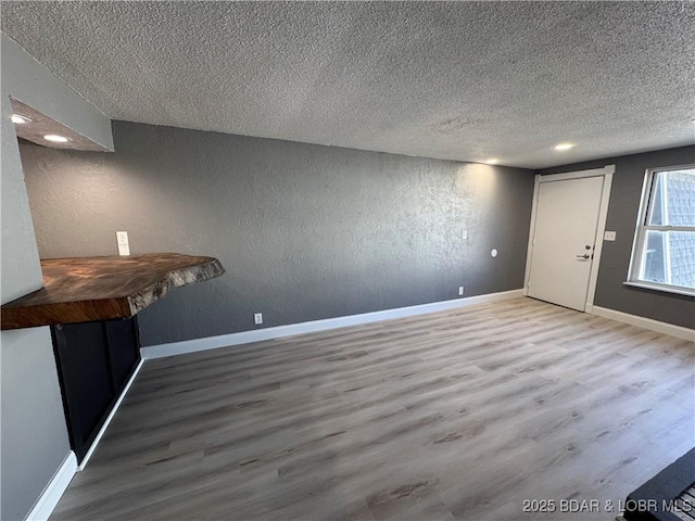 interior space with a textured wall, a textured ceiling, baseboards, and wood finished floors