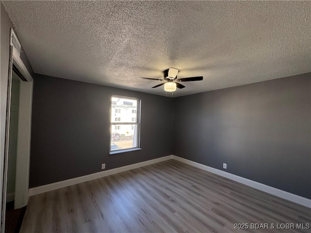 spare room with a textured ceiling, wood finished floors, a ceiling fan, and baseboards