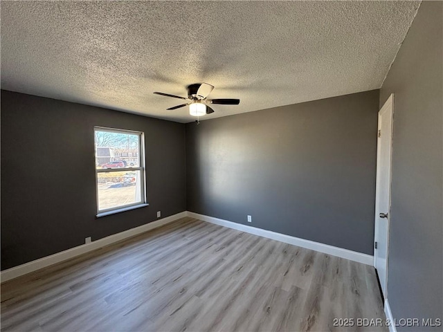 spare room with light wood-style flooring, baseboards, ceiling fan, and a textured ceiling