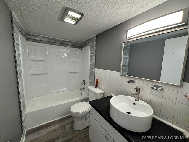 full bathroom with toilet, wood finished floors, a textured ceiling, shower / washtub combination, and tile walls