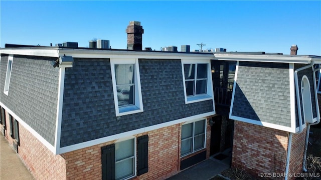 rear view of property with a shingled roof, brick siding, mansard roof, and central AC unit