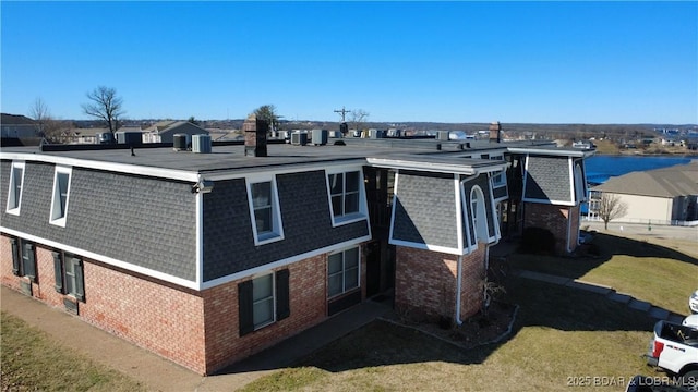 exterior space with a shingled roof, a front yard, and brick siding