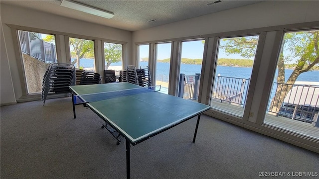 recreation room with a water view, carpet, visible vents, and a textured ceiling