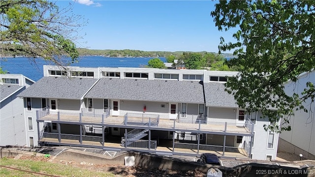 rear view of house featuring a shingled roof and a deck with water view