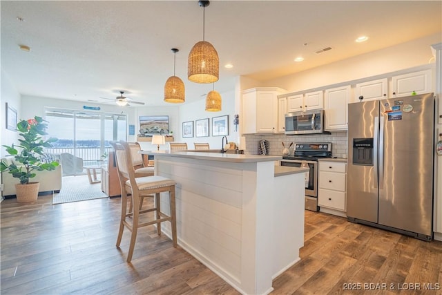 kitchen featuring stainless steel appliances, wood finished floors, visible vents, white cabinetry, and tasteful backsplash