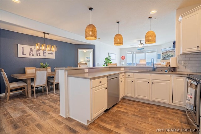 kitchen with stainless steel appliances, wood finished floors, a peninsula, and a sink