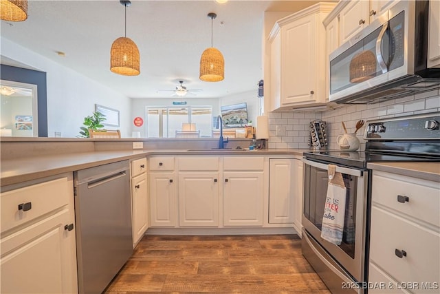 kitchen featuring wood finished floors, hanging light fixtures, a sink, stainless steel appliances, and backsplash