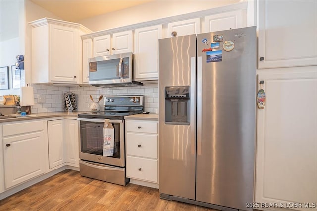 kitchen featuring light wood finished floors, white cabinetry, appliances with stainless steel finishes, and decorative backsplash