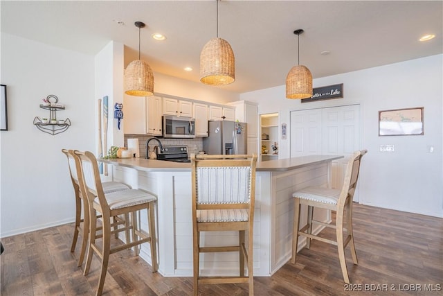 kitchen with dark wood-style floors, a breakfast bar area, decorative backsplash, appliances with stainless steel finishes, and a peninsula