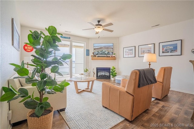 living area with visible vents, dark wood-type flooring, a large fireplace, ceiling fan, and baseboards