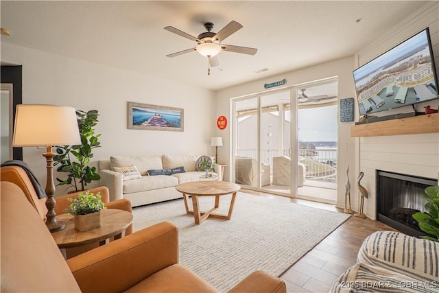 living room with a ceiling fan, a fireplace, and wood finished floors